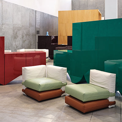 Two low armchairs with cream backs, green seats and tan bases beside tall red and green cabinets