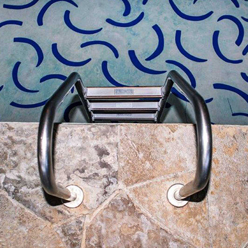 A stainless steel pool ladder with three steps set into a stone-tiled edge above teal water with blue crescent shapes