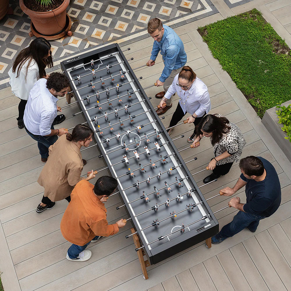 Eight people play on a large foosball table on an outdoor patio