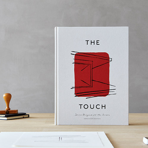 A white hardcover book titled The Touch with a red block and black line drawing, standing on a wooden desk