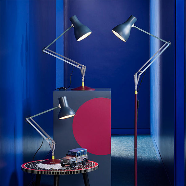 Three slate grey angled desk and floor lamps with burgundy bases against deep blue walls