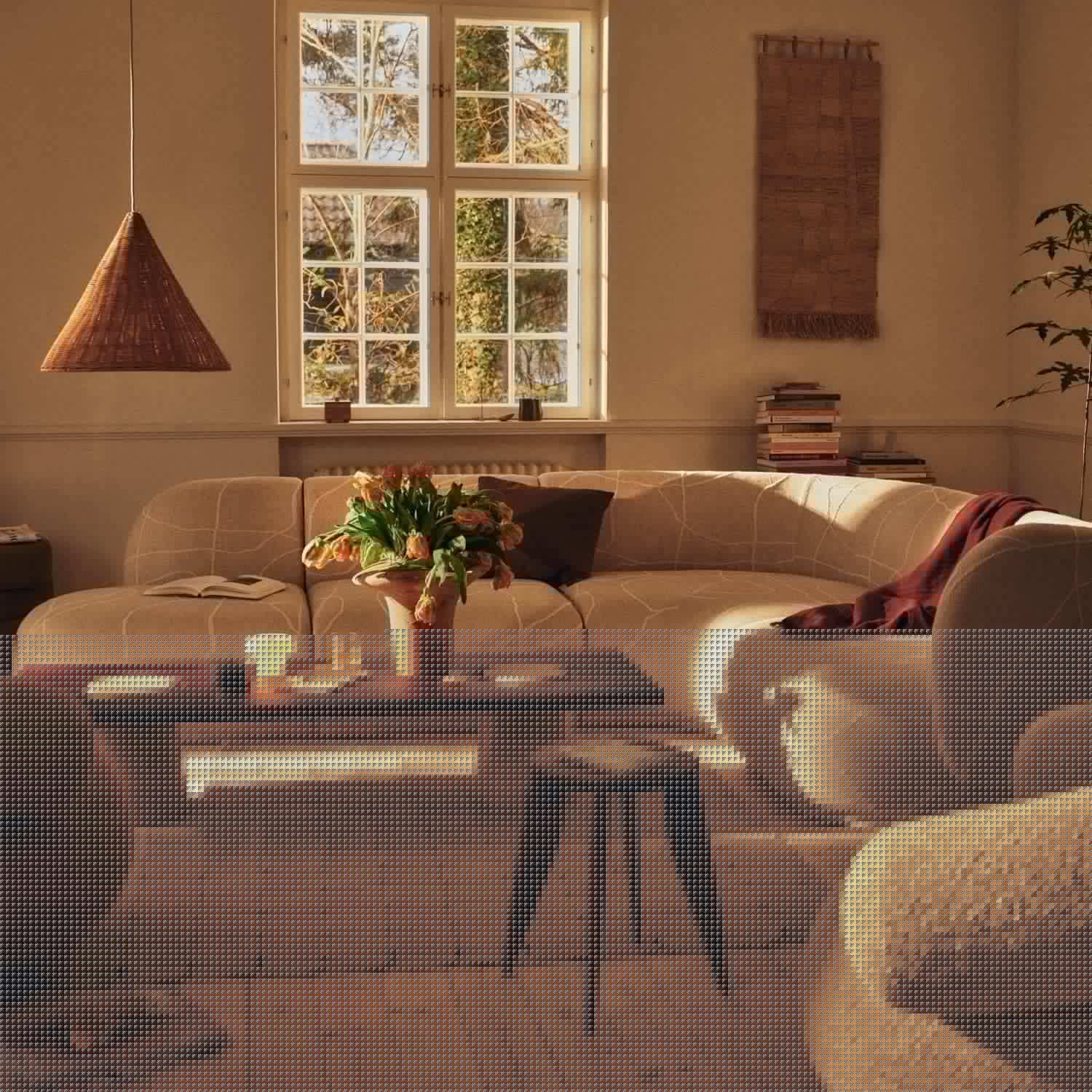 A curved cream sofa with a veined pattern in a sunlit room, under a woven cone pendant lamp