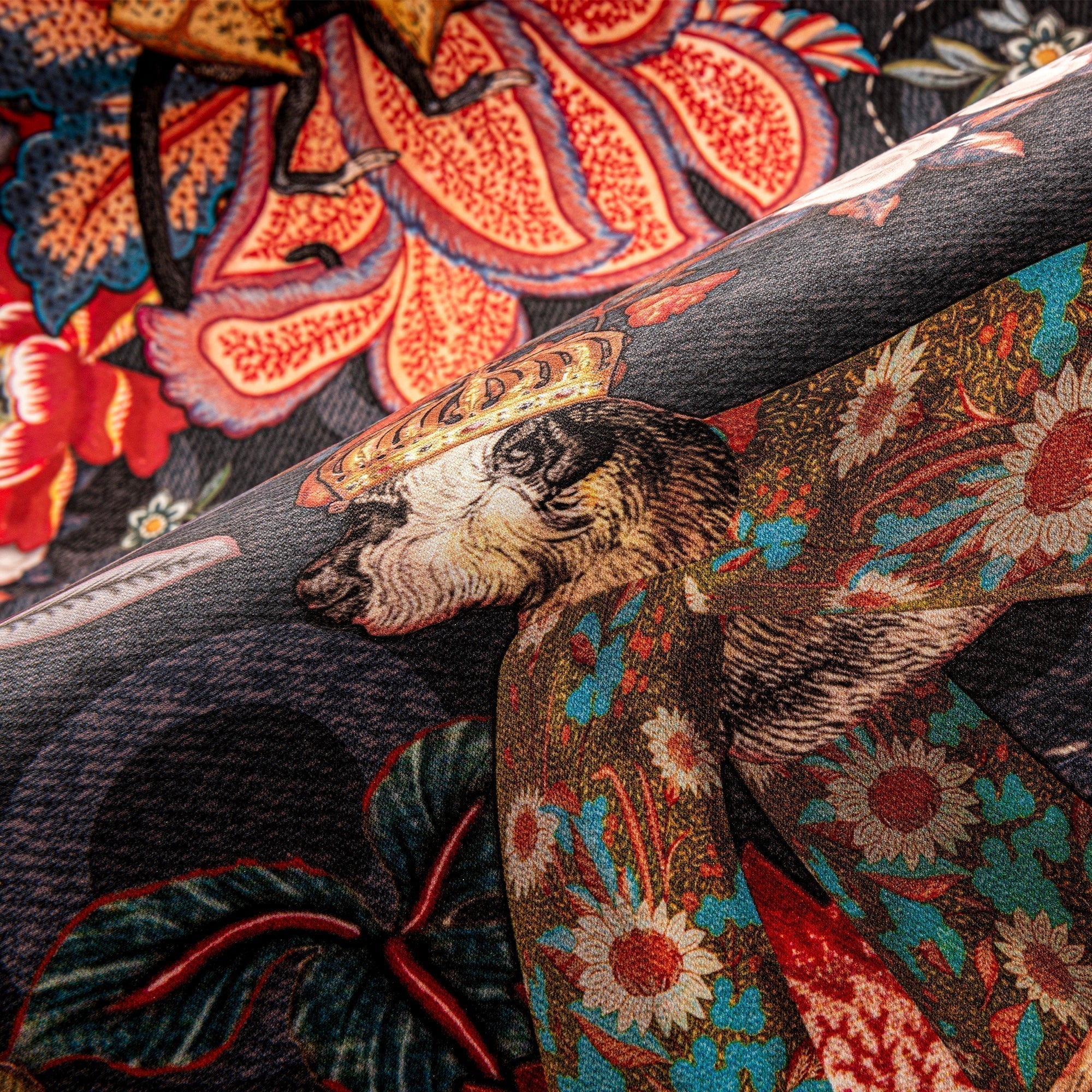 Close-up of folded dark grey fabric printed with a crowned monkey, large orange flowers and teal leaves