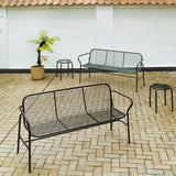 Black metal mesh Vig dining bench with slender frame on light brick patio.