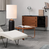 A round glass-topped coffee table with a tan leather frame, beside a cream chaise and a black stone lamp