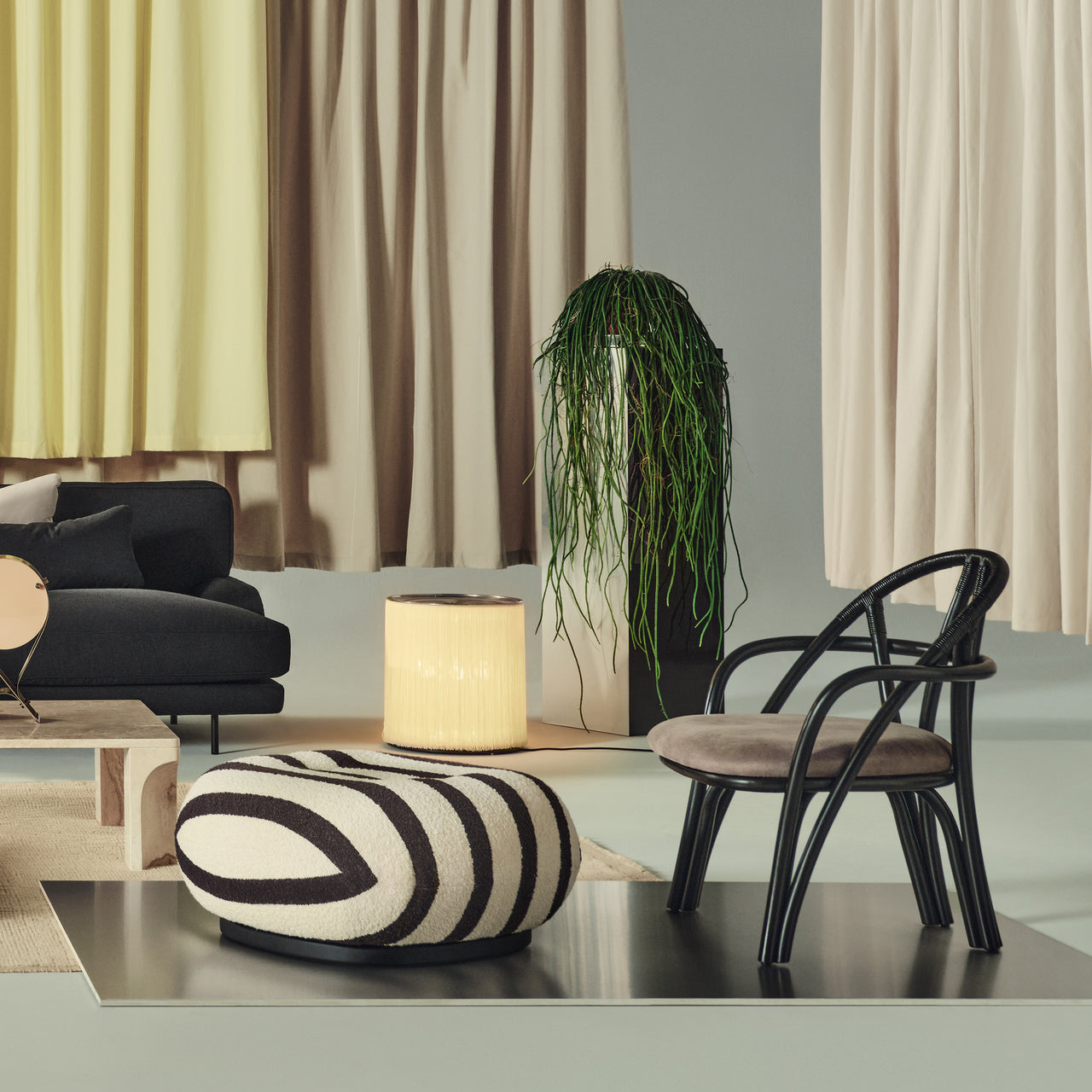 A black bentwood lounge chair with a rounded back and taupe padded seat beside a striped ottoman