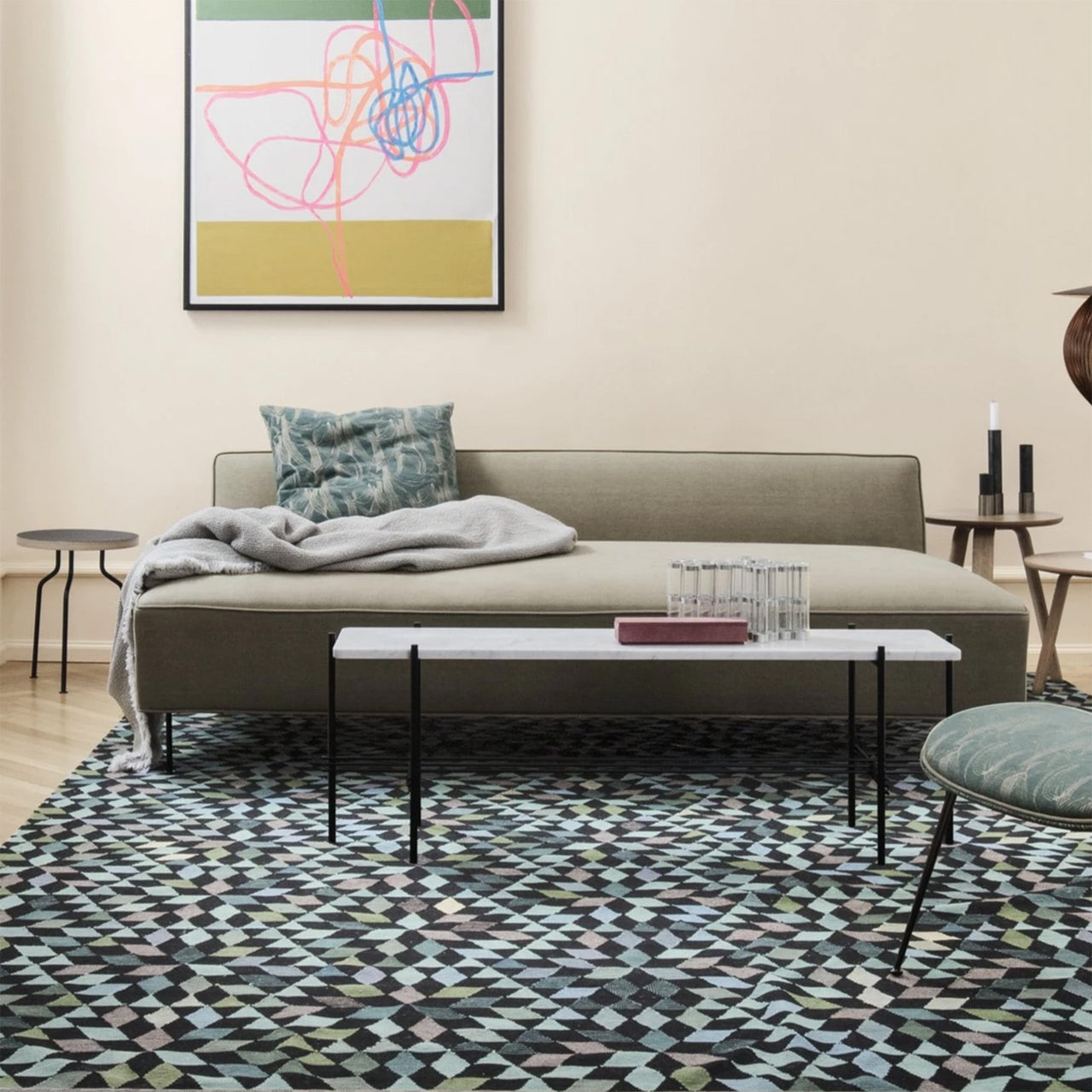 A low olive-green sofa with a grey throw, in a living room with a white marble coffee table and patterned rug