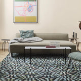 A low olive-green sofa with a grey throw, in a living room with a white marble coffee table and patterned rug