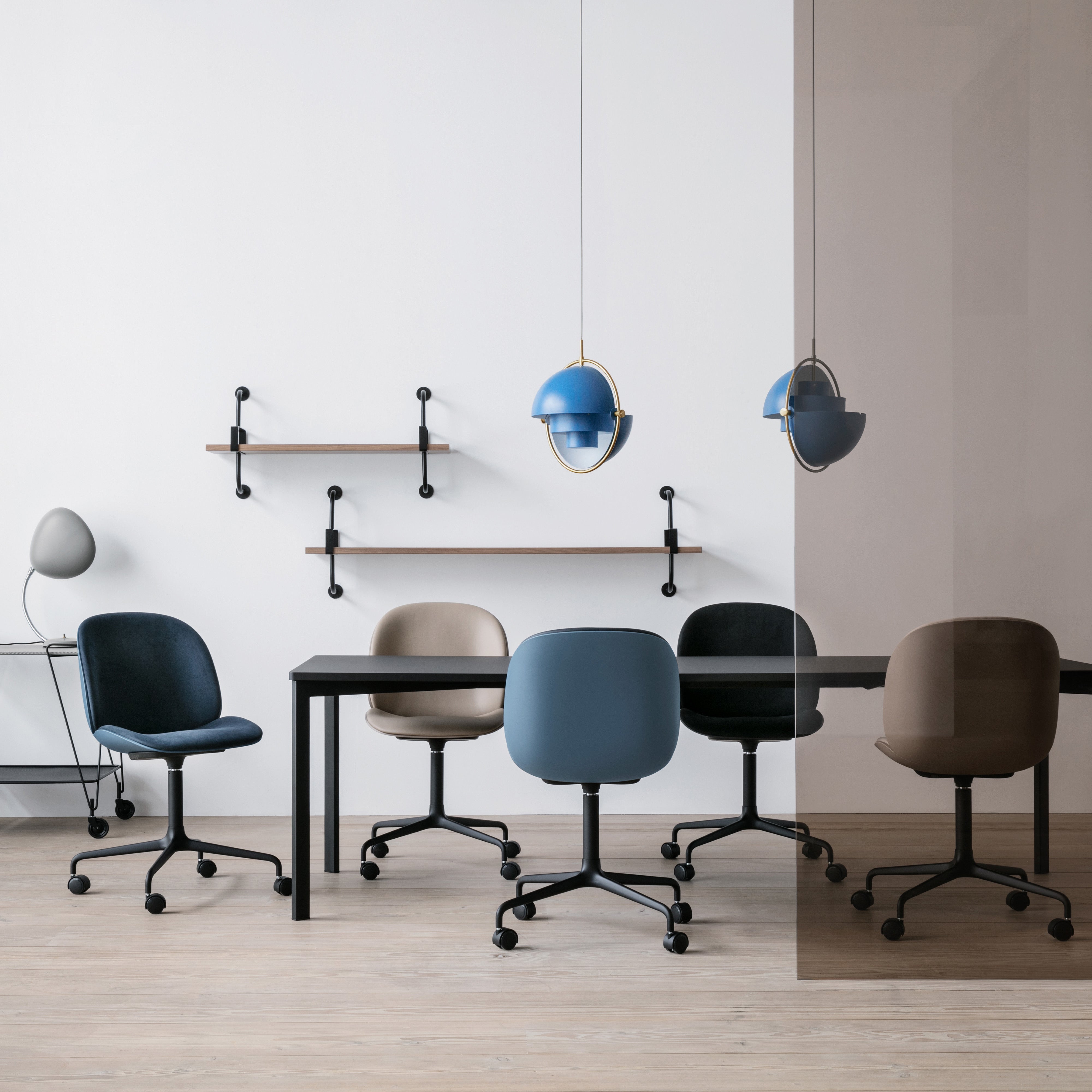 A blue pendant light with brass ring hangs over a black table and five swivel chairs on casters