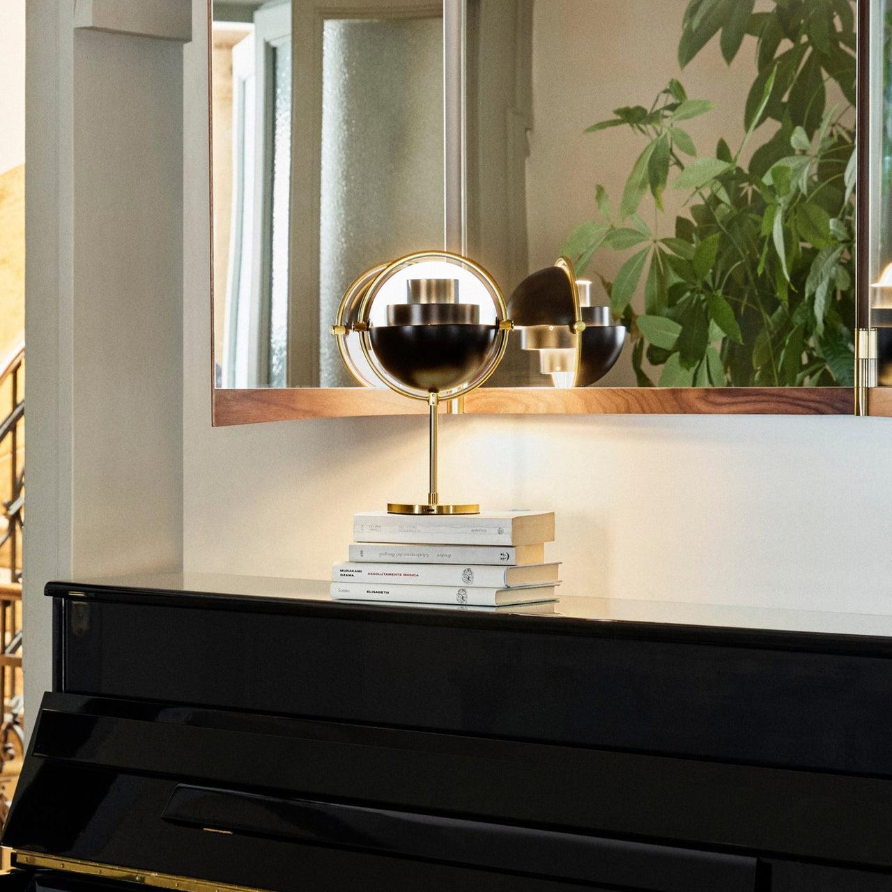 A small brass lamp with a black half-dome shade, glowing on books atop a black piano