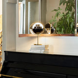 A small brass lamp with a black half-dome shade, glowing on books atop a black piano