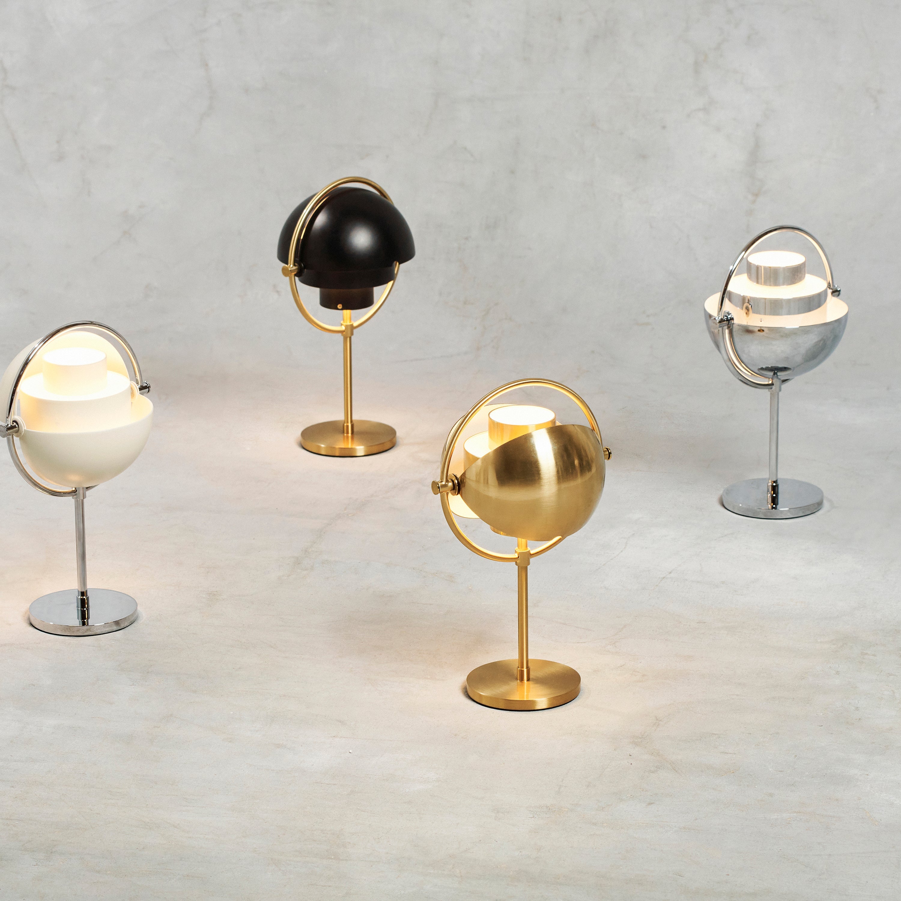 Four table lamps with tilting half-dome shades in brass, black, cream and chrome on a grey surface