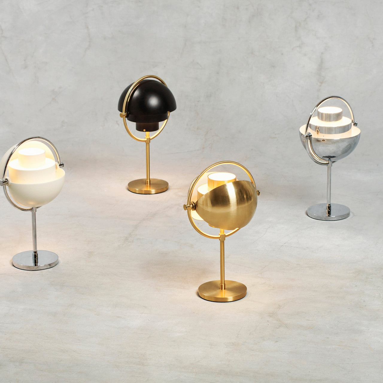 Four table lamps with tilting half-dome shades in brass, black, cream and chrome on a grey surface