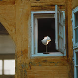 A small white lamp with layered rotating shades glows in an open window of an old ochre timber-framed wall