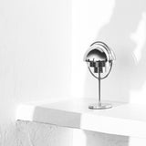 A small chrome table lamp with a half-dome shade on a thin stem, on a white ledge