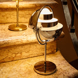 A glowing chrome table lamp with a rounded, tilting shade on a round base, sitting on marble stairs