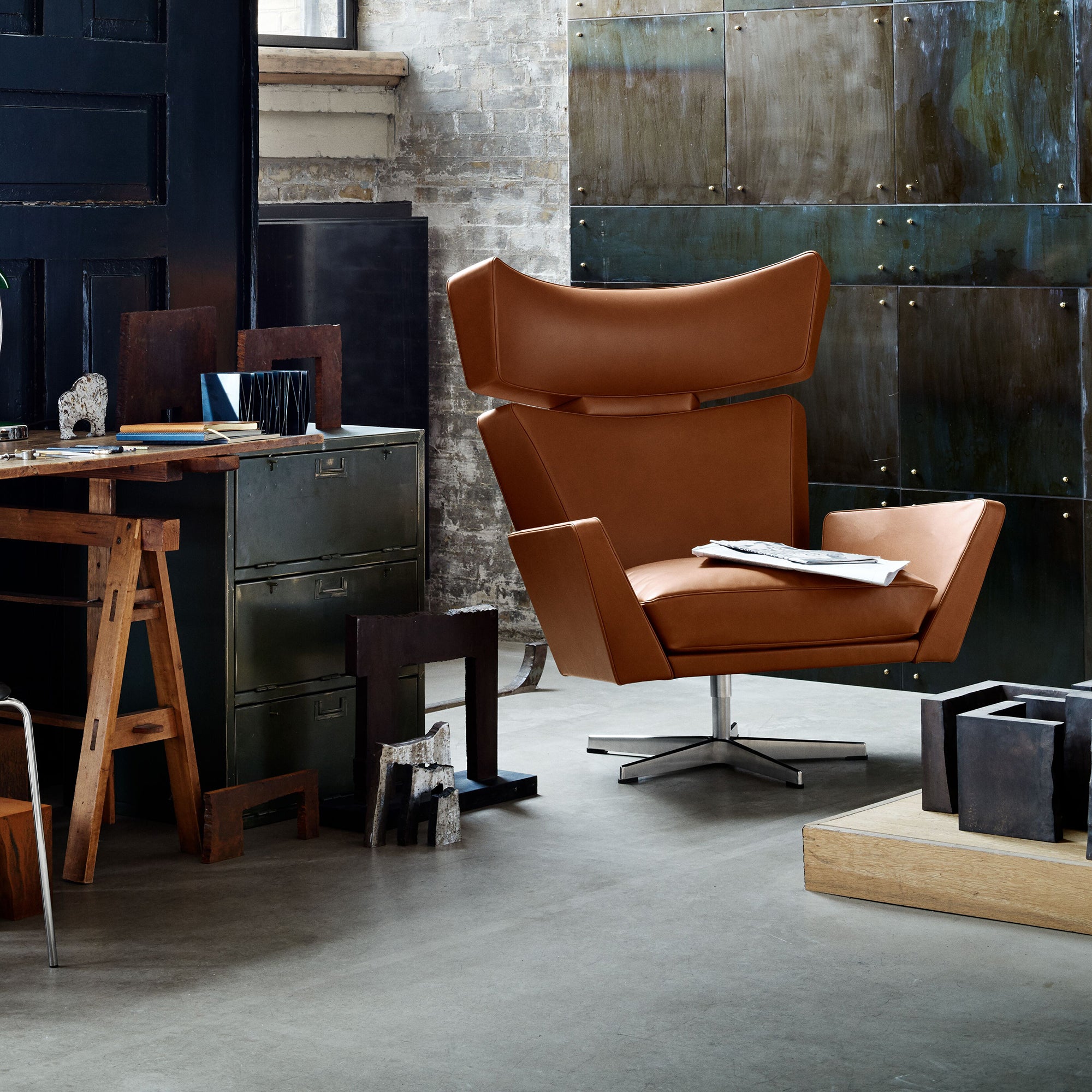 A tan leather swivel lounge chair with angular wings and a chrome star base in an industrial studio