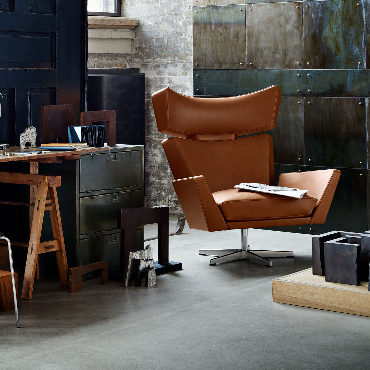 A tan leather swivel lounge chair with angular wings and a chrome star base in an industrial studio
