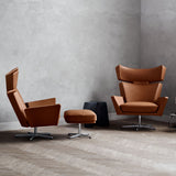 Two tan leather high-back swivel chairs and a matching ottoman on steel bases in a grey room