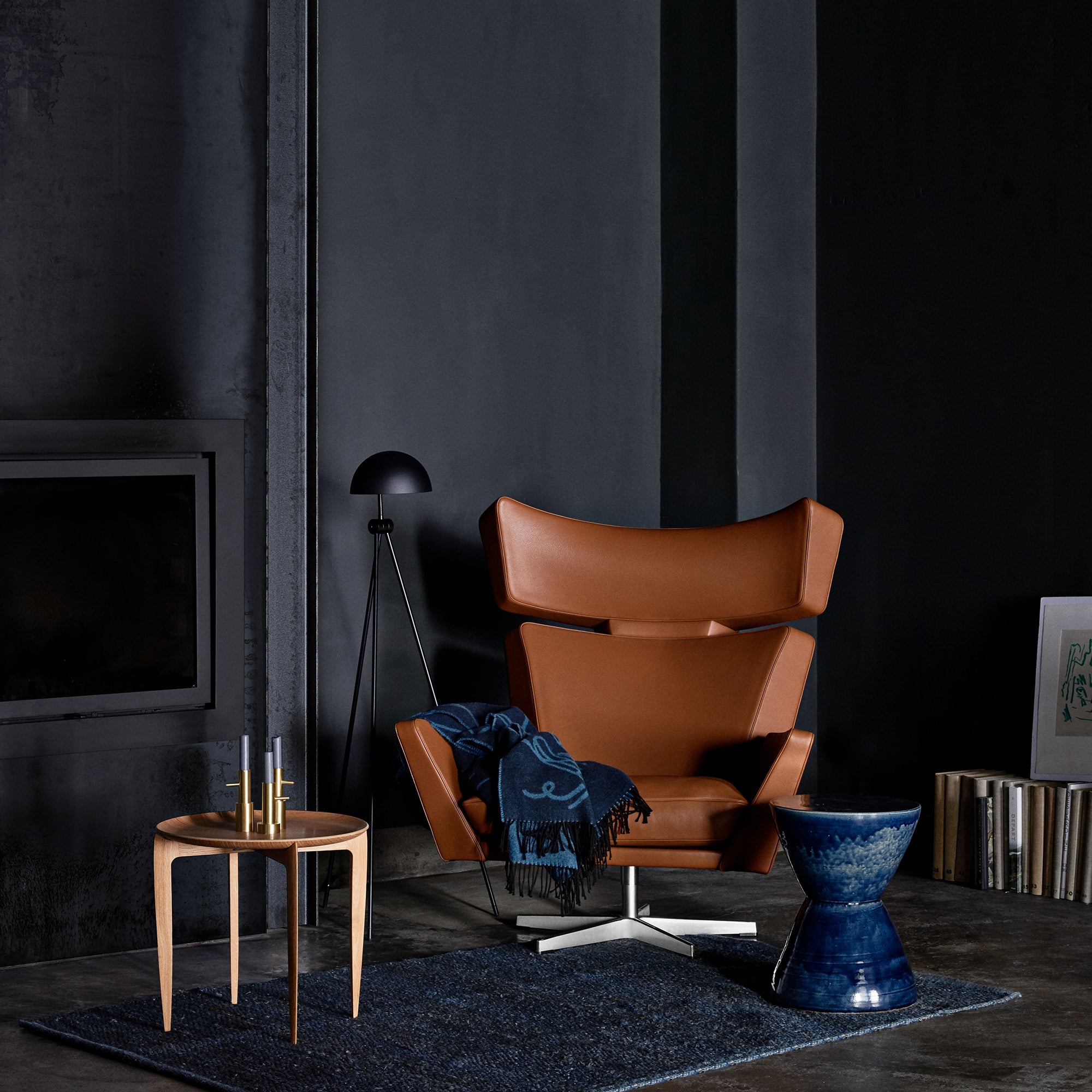 A tan leather wing chair on a swivel base with a blue throw, in a dark room