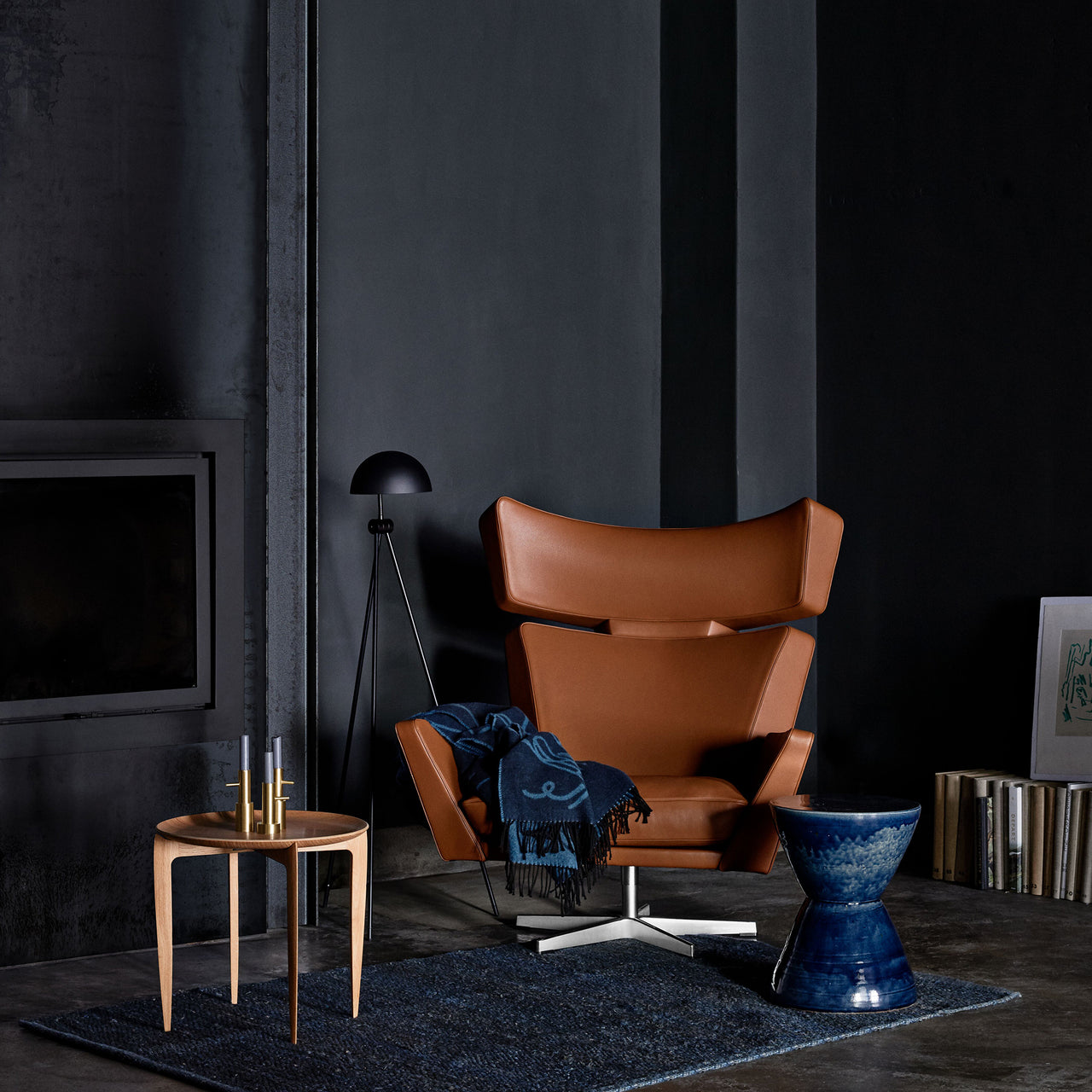 A tan leather wing chair on a swivel base with a blue throw, in a dark room