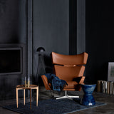 A tan leather wing chair on a swivel base with a blue throw, in a dark room