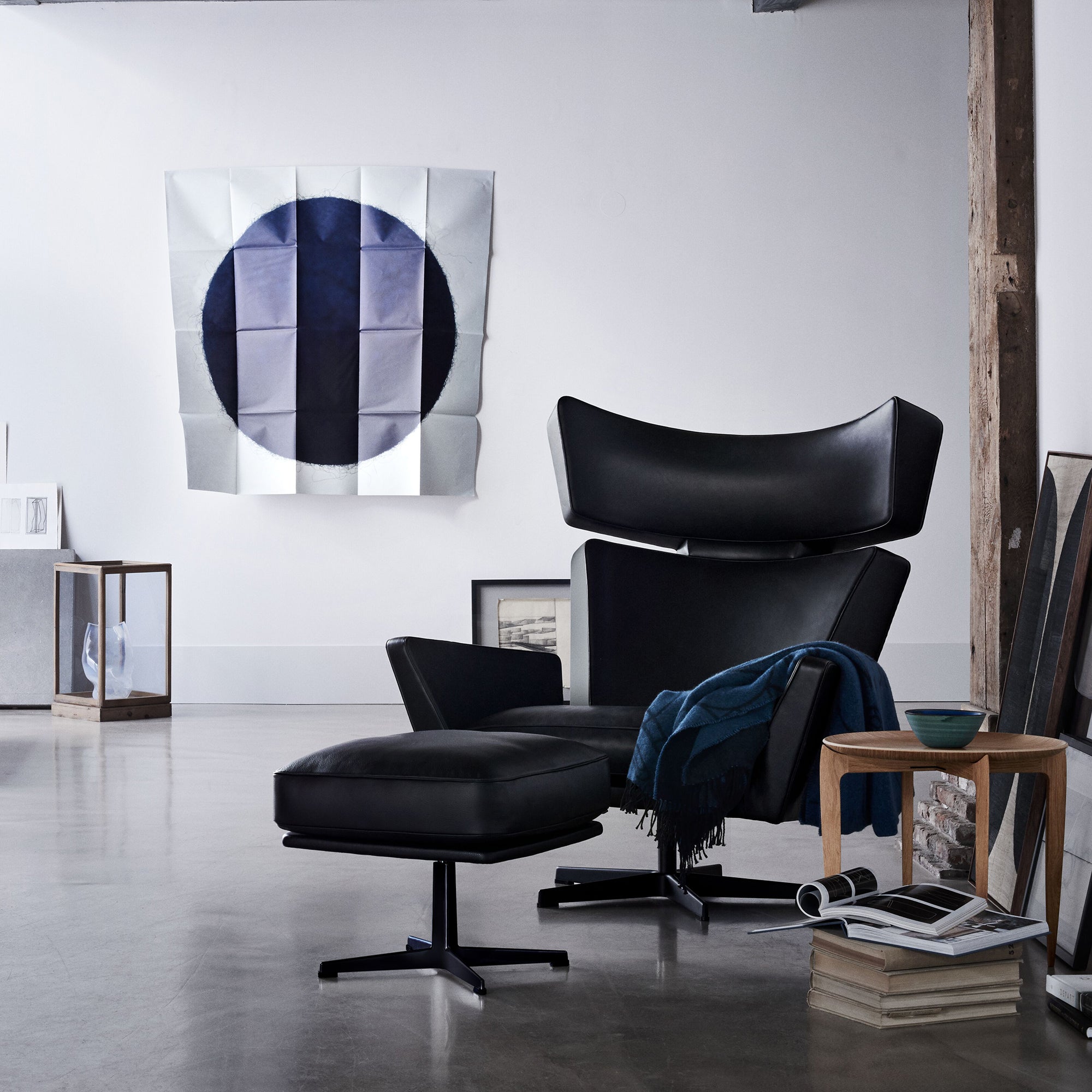 A black leather lounge chair with winged headrest and matching ottoman in a loft with a blue throw