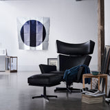 A black leather lounge chair with winged headrest and matching ottoman in a loft with a blue throw