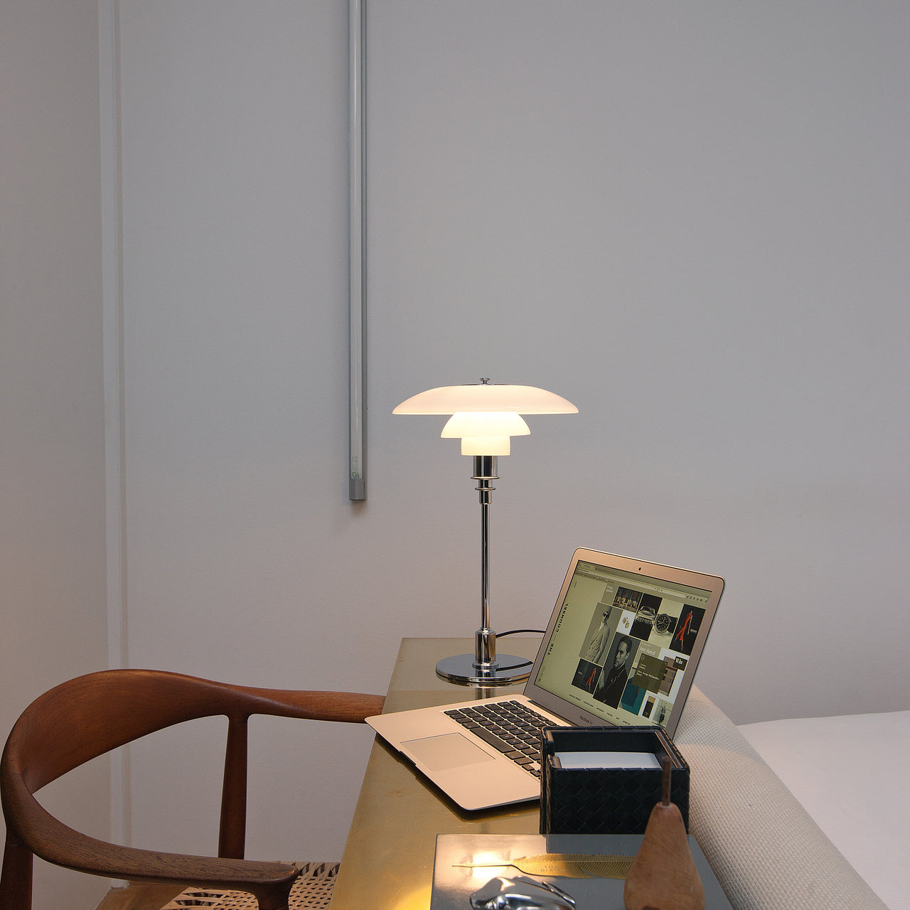 A glowing table lamp with layered white glass shades on a chrome stem, on a brass desk with a laptop