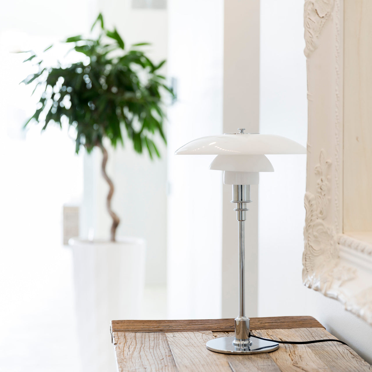 A table lamp with three layered white glass shades on a slim chrome stem, on a weathered wooden console