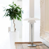 A table lamp with three layered white glass shades on a slim chrome stem, on a weathered wooden console