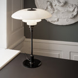 A table lamp with three layered white glass shades on a slim black stem and round base, on a dark desk