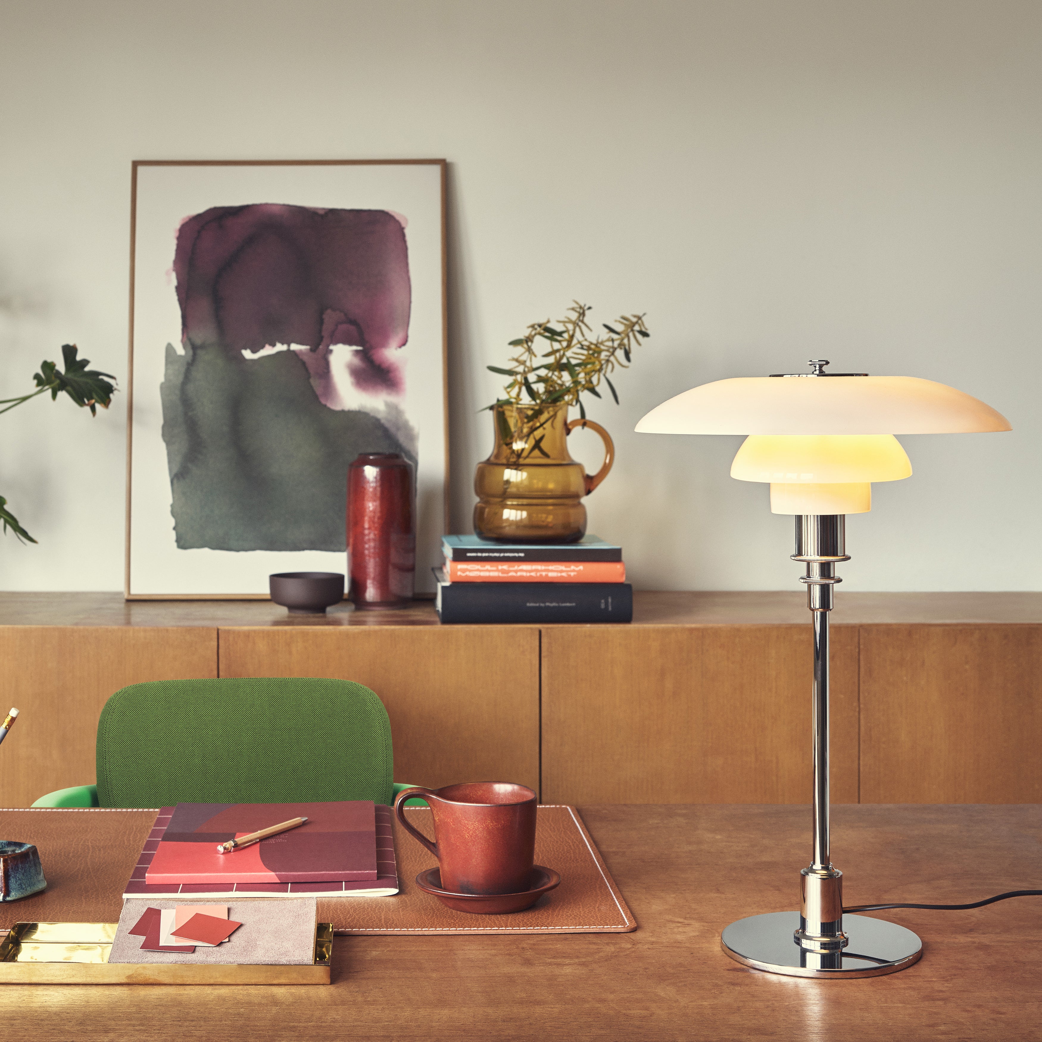 A table lamp with three layered white glass shades on a chrome stem, on a wooden desk