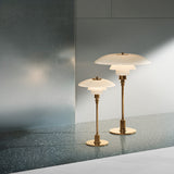 Two glowing brass table lamps with layered white glass shades, one taller, on a speckled grey floor
