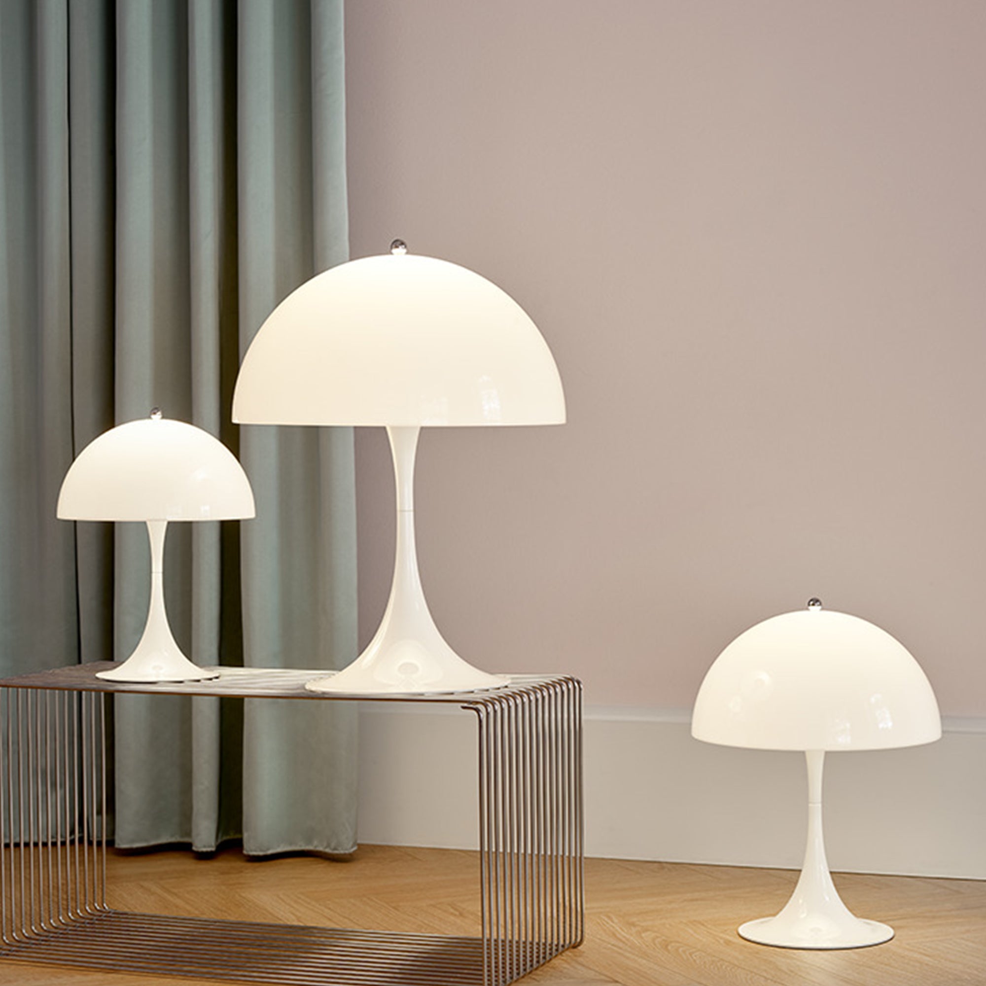 Three white dome-shaped table lamps on flared stems, two on a wire shelf and one on a wood floor