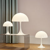 Three white dome-shaped table lamps on flared stems, two on a wire shelf and one on a wood floor