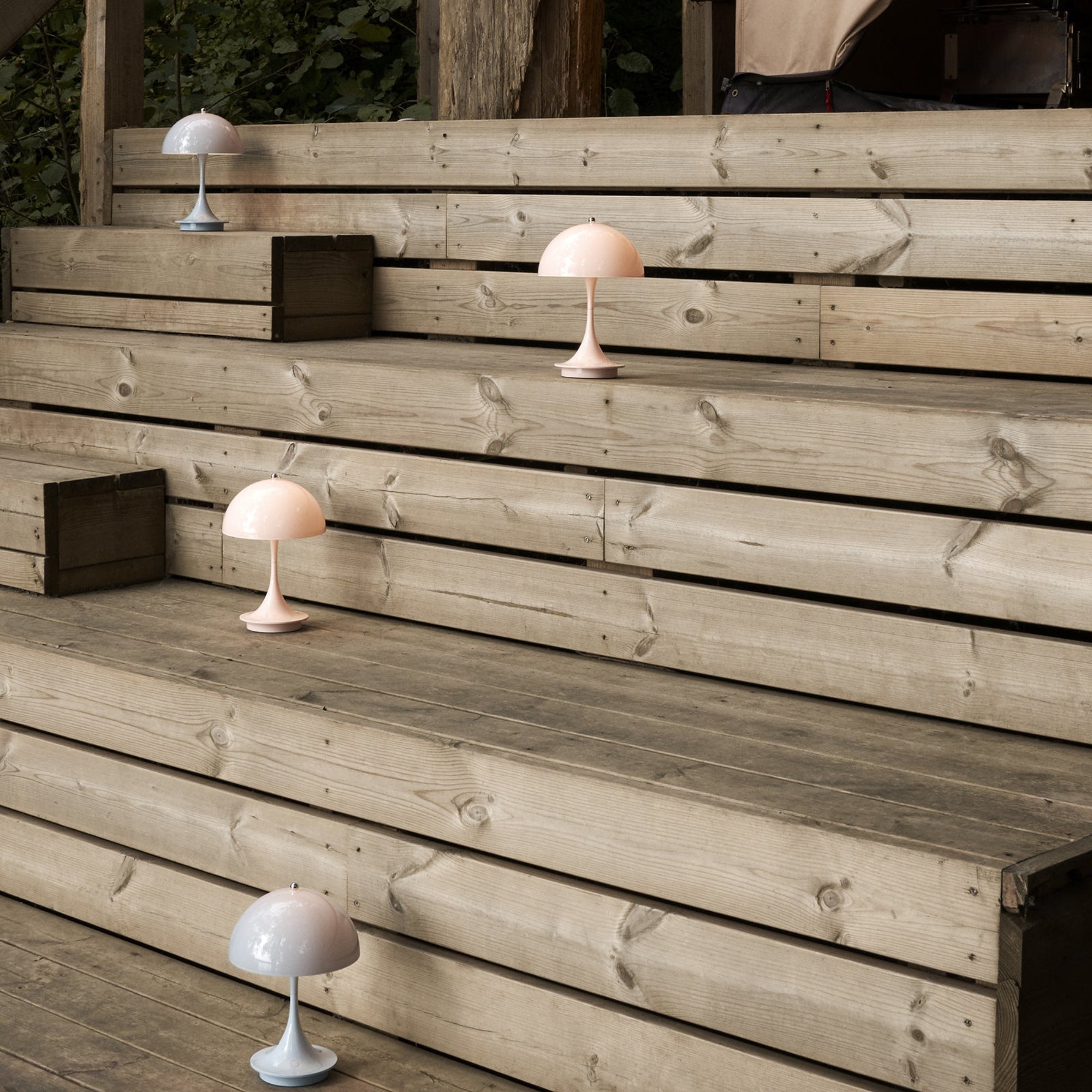 Four small mushroom-shaped table lamps in pale pink and grey on weathered wooden outdoor steps
