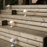 Four small mushroom-shaped table lamps in pale pink and grey on weathered wooden outdoor steps