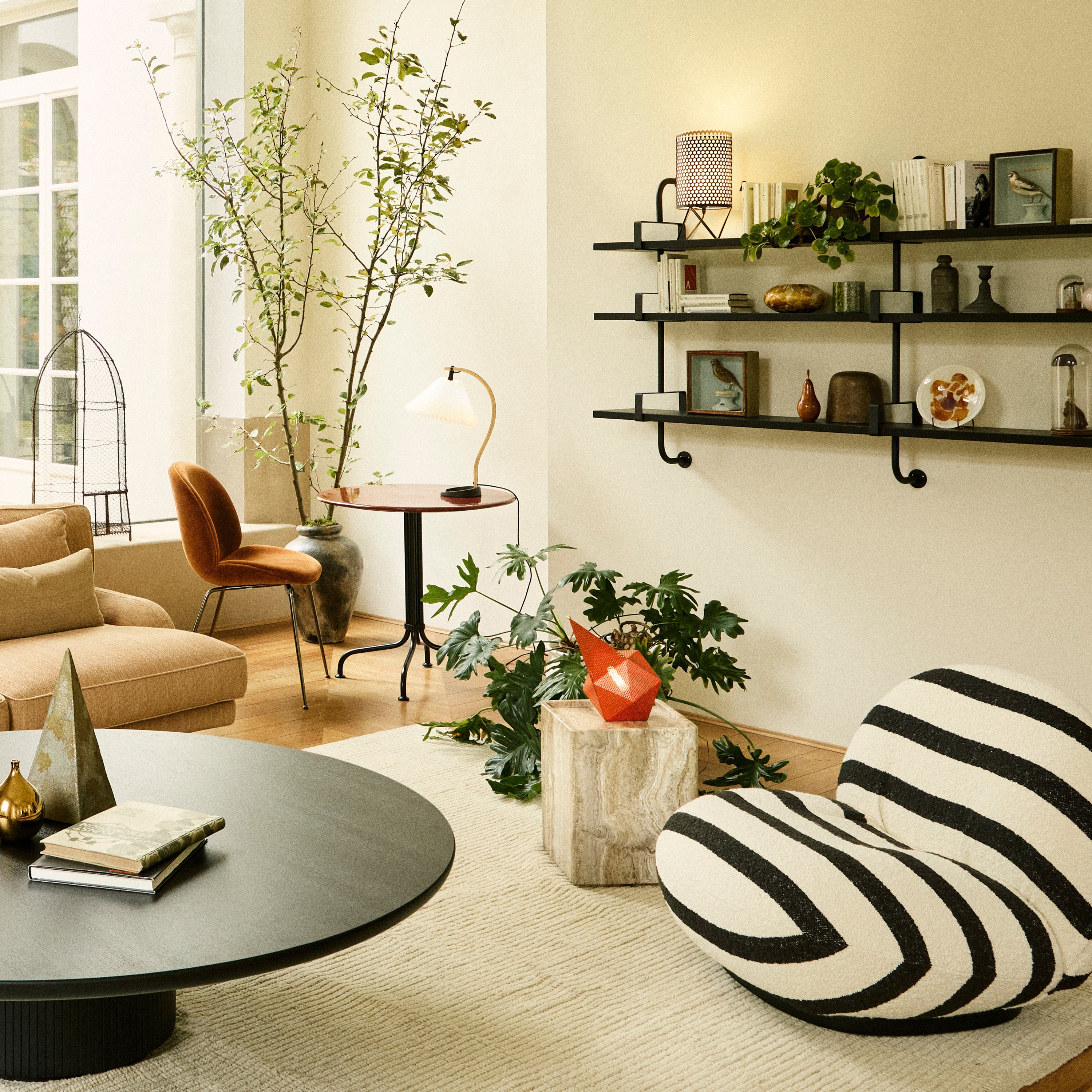 A square travertine side table beside a striped lounge chair in a bright living room with a round black table