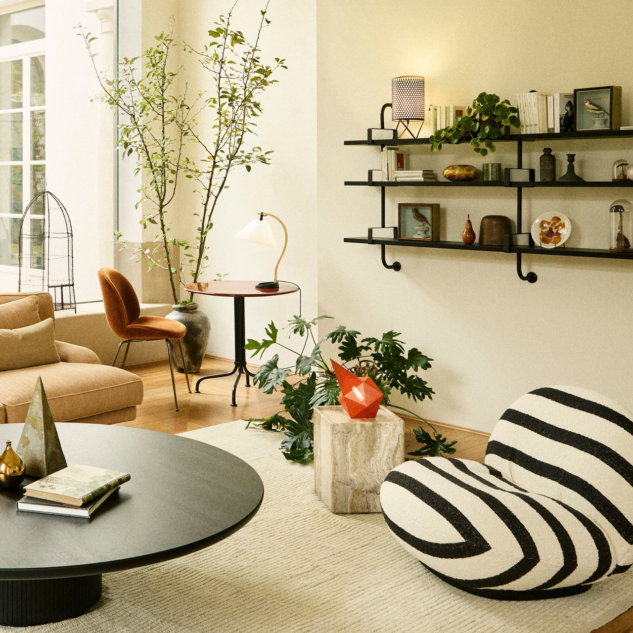A square travertine side table beside a striped lounge chair in a bright living room with a round black table