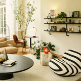 A square travertine side table beside a striped lounge chair in a bright living room with a round black table