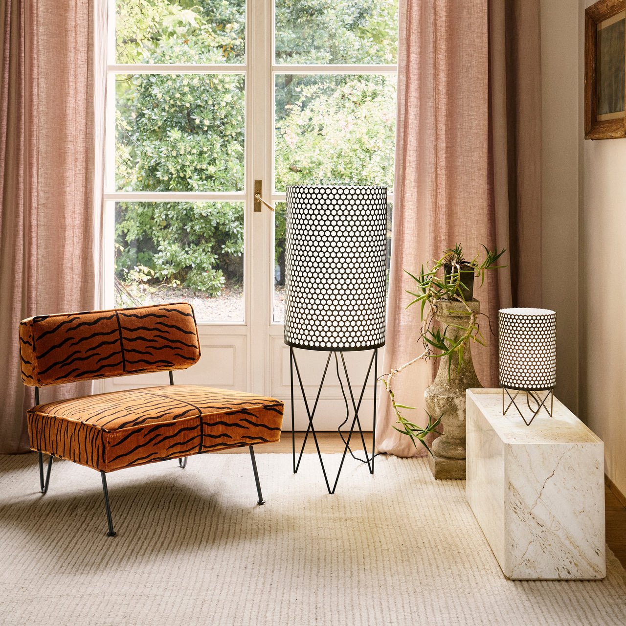 A cream marble side table holding a small perforated lamp, beside a tiger-print chair and tall floor lamp