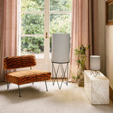 A cream marble side table holding a small perforated lamp, beside a tiger-print chair and tall floor lamp