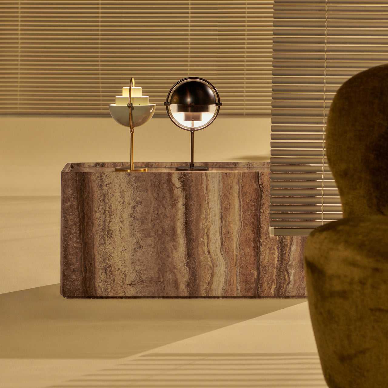 A low rectangular side table in brown veined stone holds two small table lamps, one brass and one dark