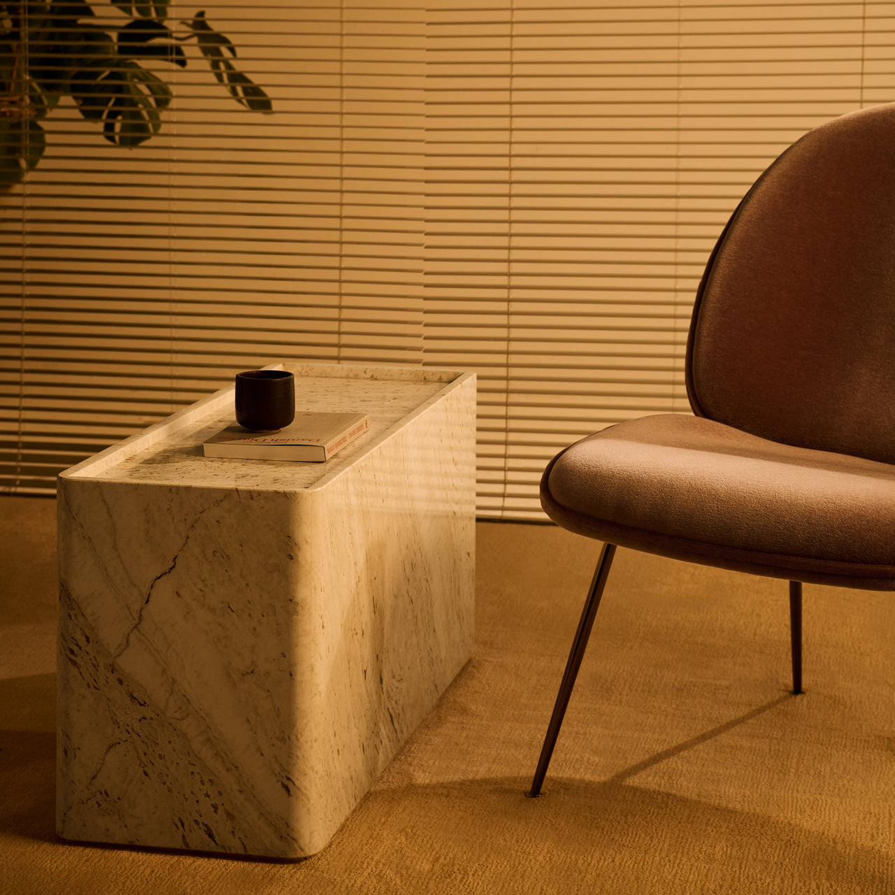 A rectangular side table in pale veined stone with rounded edges, beside a rust-brown lounge chair