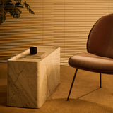 A rectangular side table in pale veined stone with rounded edges, beside a rust-brown lounge chair