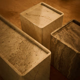 Overhead close-up of three square stone side tables in cream and grey-brown travertine with raised rims