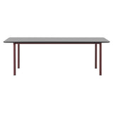 A rectangular table with a grey top and rounded corners on four slim burgundy metal legs