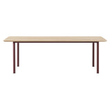 A rectangular table with a light oak top and four slim burgundy metal legs
