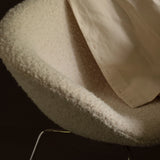 Close-up of a curved cream bouclé chair shell on thin chrome legs with a cloth draped over it